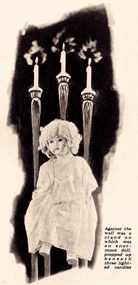 A doll in a white dress sits propped against three lighted candles.